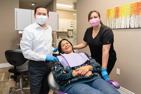 A woman in dental chair with Dr. Le and a dental assistant.