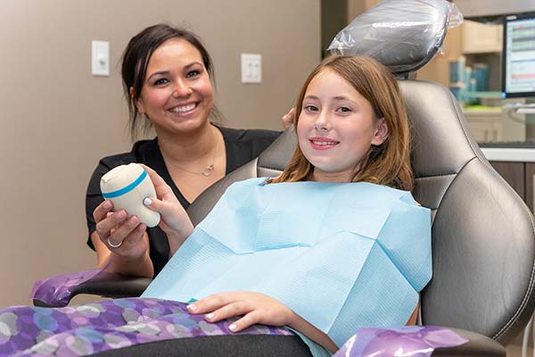 A girl in a dental chair smiling with a dental assistant handing her a toy.