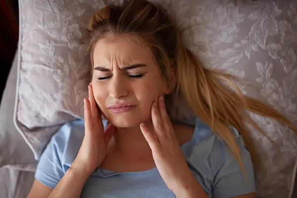 Woman suffering from bruxism and rubbing her jaw while in bed.Picasso Dental Care in Temecula, CA Woman suffering from bruxism and rubbing her jaw while in bed.Picasso Dental Care in Temecula, CA