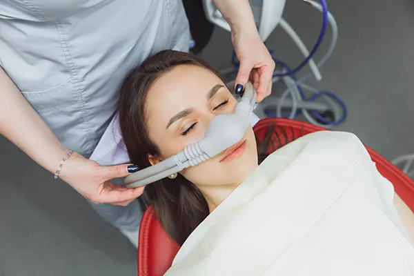 Dental assistant fitting a sedation mask over the nose of her calm female patient at Picasso Dental Care in Temecula, CA 
